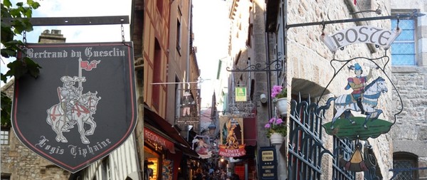 Enseigne de la maison du Chevalier Du Gesclin  © Catherine Gary ; La ruelle qui conduit à l'Abbaye.  © E.Kerleroux;  Enseigne de la poste qui s’est installée en lieu et place de la première adresse de la Mère Poulard  © Catherine Gary