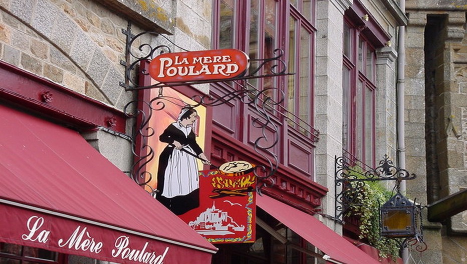 La célèbre enseigne de la Mère Poulard au Mont-Saint-Michel. La Mère Poulard reste ici une ambassadrice privilégiée par la grâce d’une omelette fameuse qui fait le succès de son auberge depuis plus de 150 ans.  © OT Mont-Saint-Michel